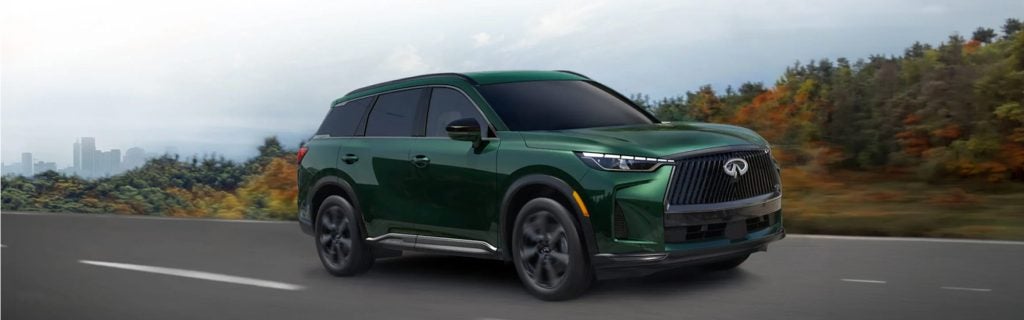 Dark green luxury SUV cruising on a scenic highway with autumn trees in the background.
