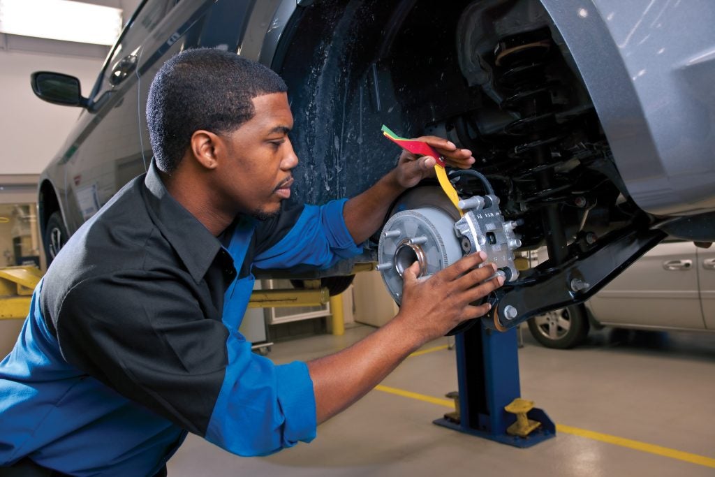 Technician inspecting and repairing a vehicle brake system in an auto service shop.