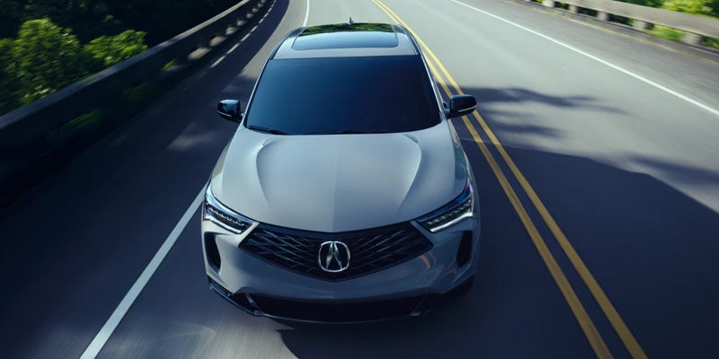 2026 Acura RDX Technology Package SUV driving on a scenic road in Grapevine, TX, featuring a sleek front grille, modern headlights, and a panoramic sunroof.