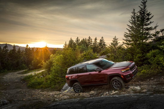 red car on rocks by a body of water during sunset