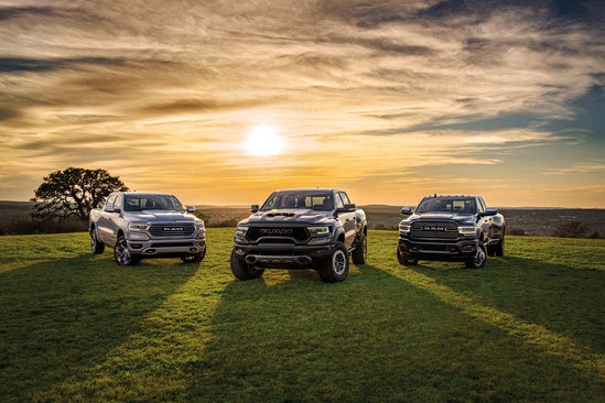 a lineup of three ram trucks in a grassy field at sunset 