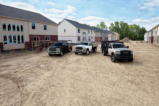 three trucks sitting in a dusty construction area near houses under construction 
