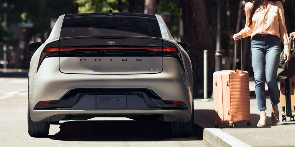 Two people with suitcases walking up to a parked 2024 Toyota Prius
