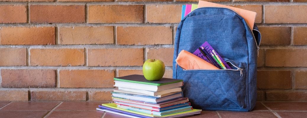 An apple atop of a stack of books and a bag