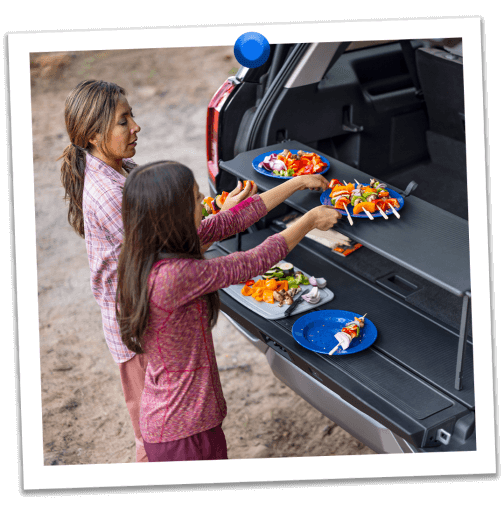 A mother and daughter prepare kebabs at their campsite on the pop‑up tailgate tabletop of their Expedition® SUV