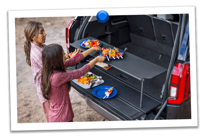 A mother and daughter prepare kebabs at their campsite on the pop‑up tailgate tabletop of their Expedition® SUV
