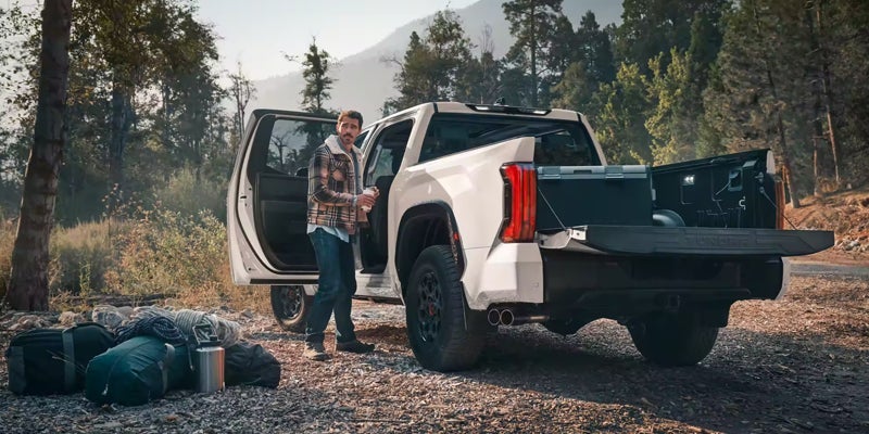 An all-new 2024 White Toyota Tundra parked in the wilderness among the trees with overnight bags and coolers packed in and around the truck. - Phil Meador Toyota Pocatello, ID