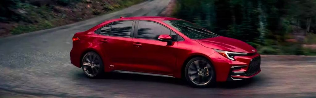 An all-new 2024 Ruby Flare Pearl Toyota Corolla Hybrid cruising through the forest backroads in Pocatello, ID.