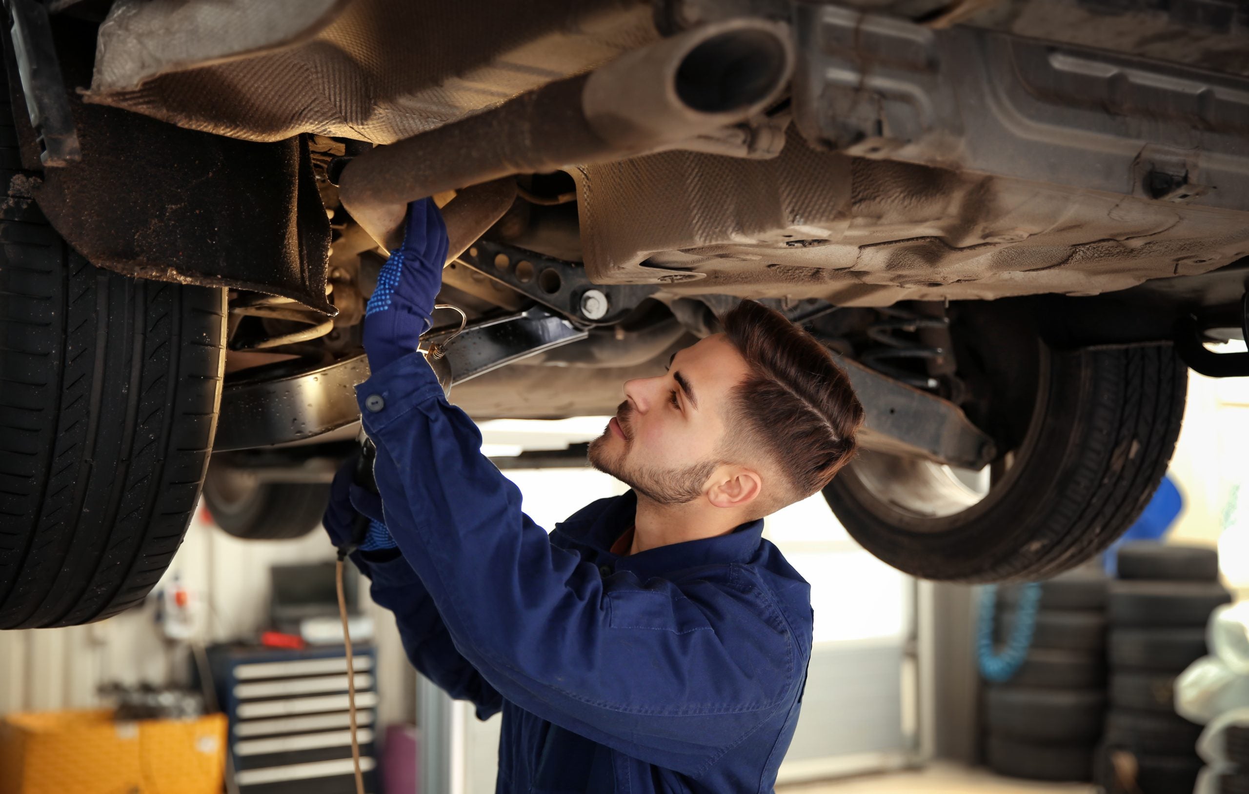 A mechanic working under a car, inspecting and repairing the exhaust system