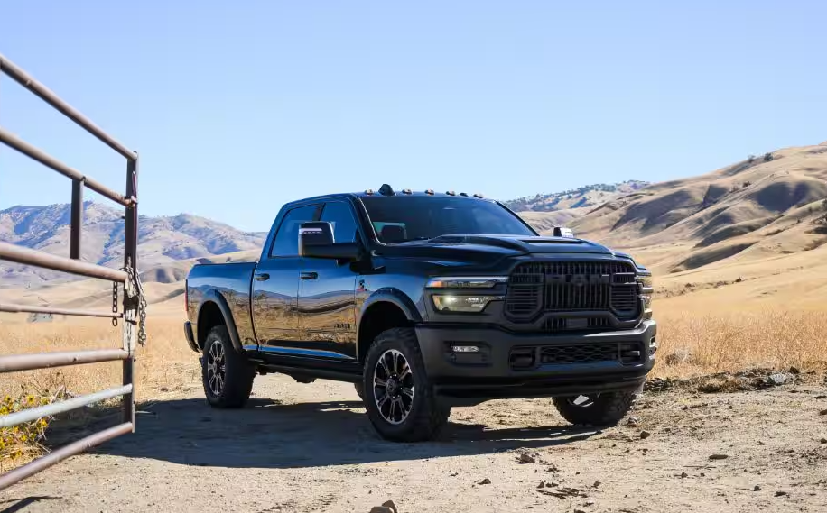A black RAM 2500 Heavy Duty pickup truck parked by a ranch gate on a dirt road