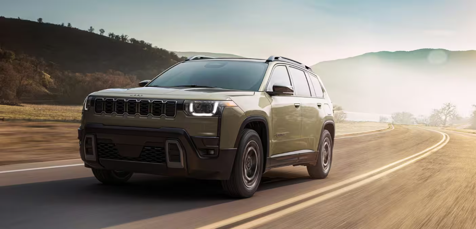 An olive green Jeep Cherokee driving on a winding paved road