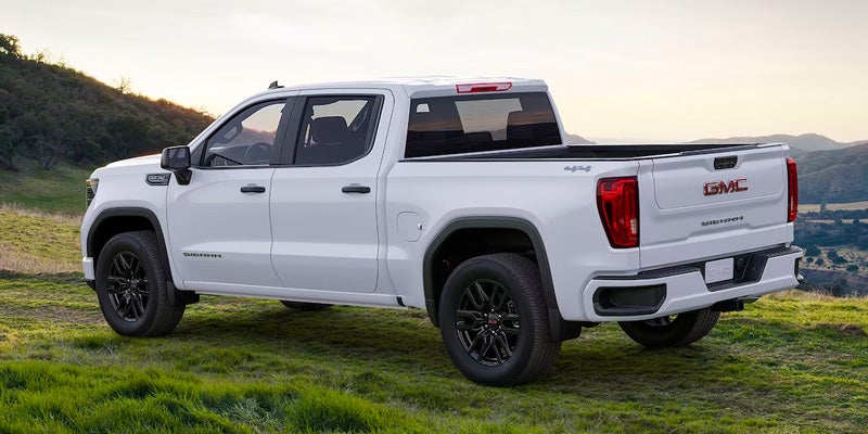 GMC pickup truck parked on grassy hillside at sunset.