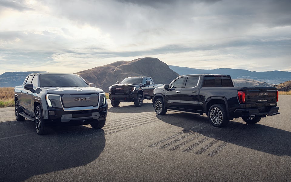 Three GMC Sierra 1500 pick-up trucks parked by each other on display with a mountain view.
