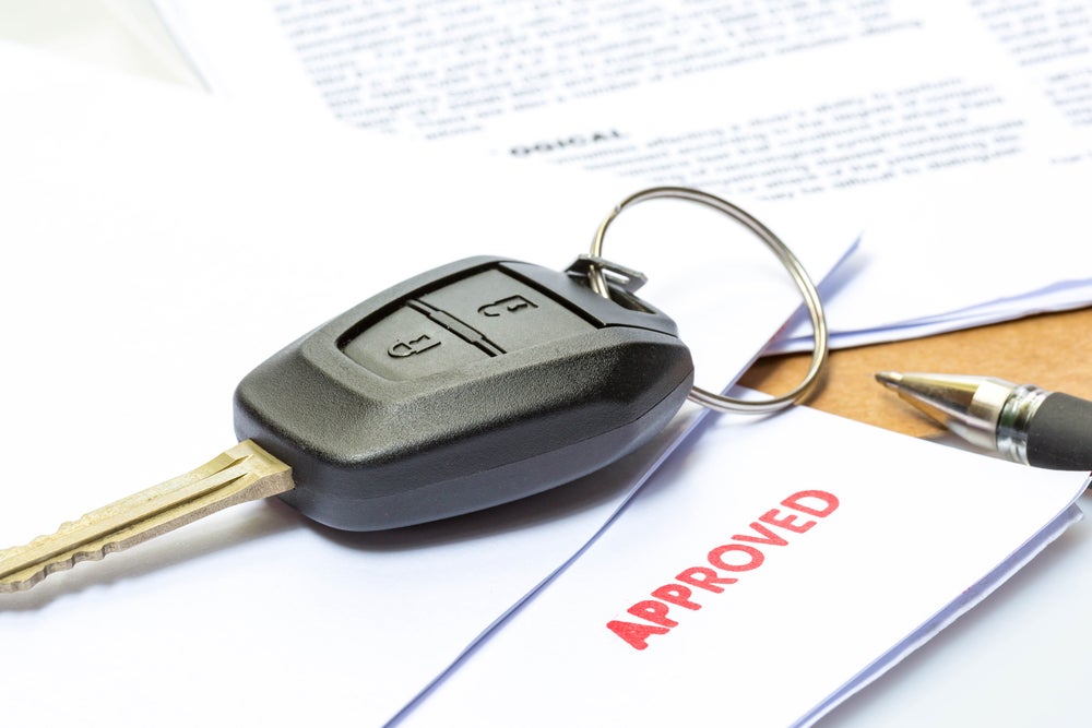 A pair of car keys sitting on top of approved automotive paperwork