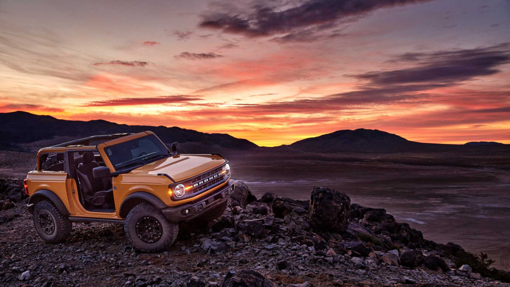 Yellow off-road SUV parked on rocky terrain at sunset, with an open top and rugged mountains in the background, conveying adventure and freedom.