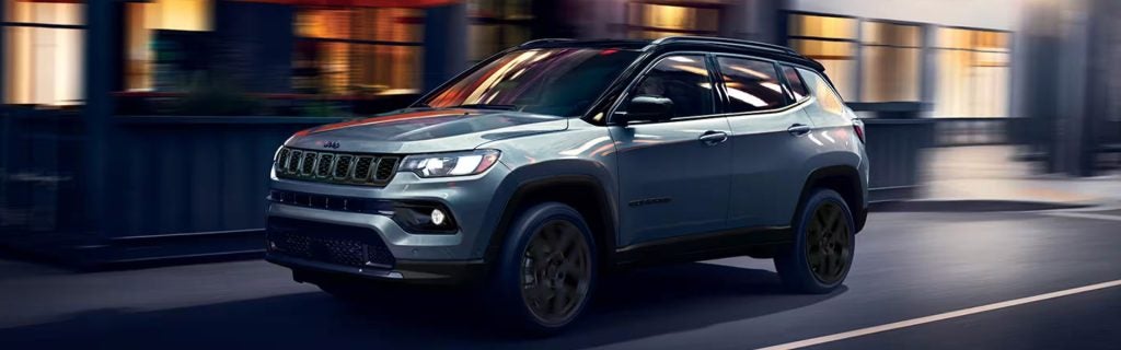 A silver Jeep Compass driving through a city at night with motion blur.