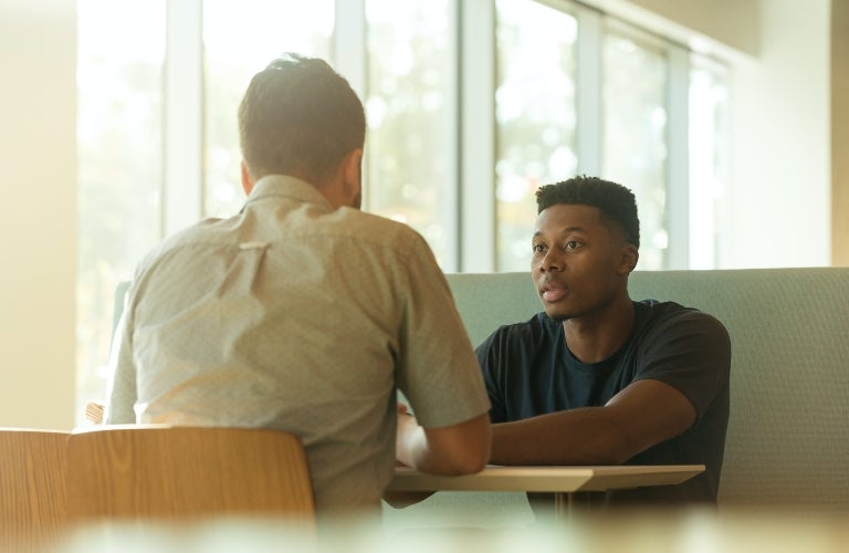 Two Men Sitting and Talking at Table by Window