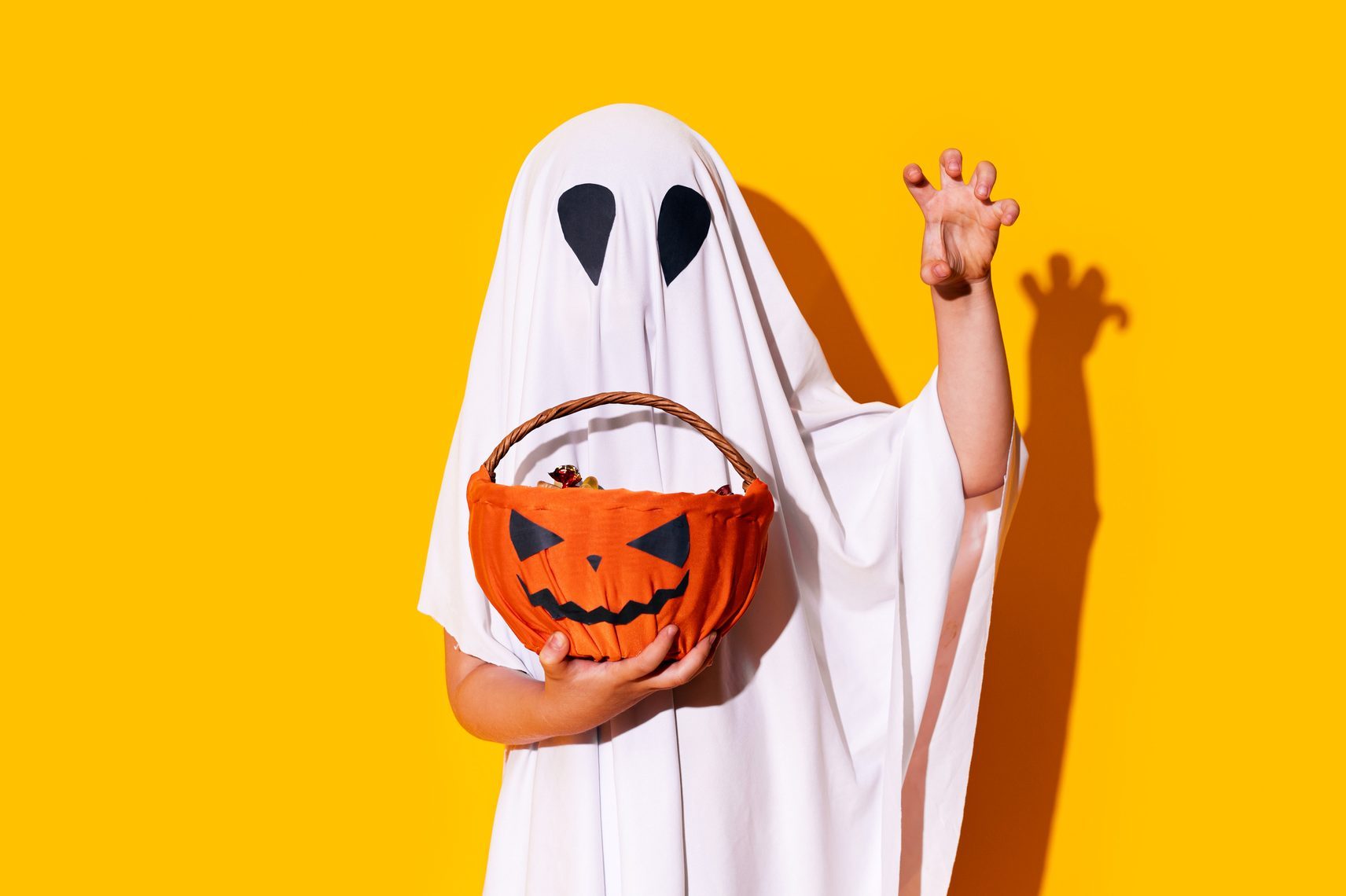 child dressed as ghost holding pumpkin