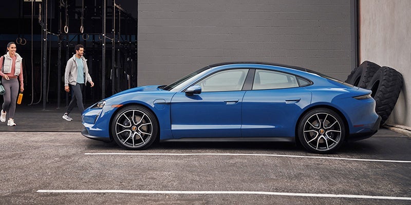 A man and a woman leaving a gym and walking toward a blue 2024 Porsche Taycan Cross Turismo
