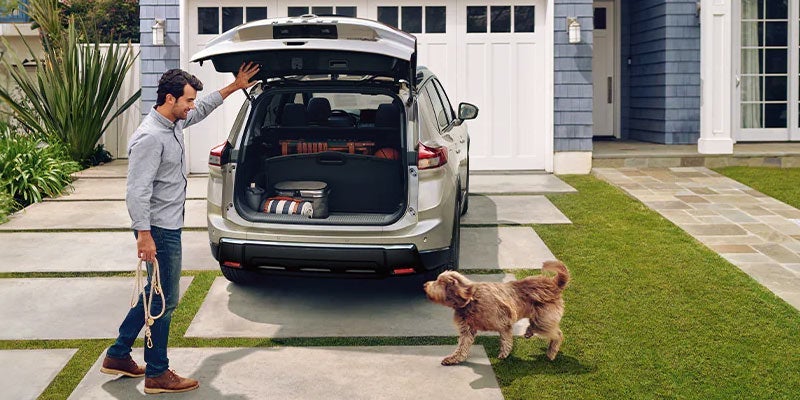 A guy preparing for a road trip with his dog in his 2024 Nissan Rogue near San Leandro, CA 