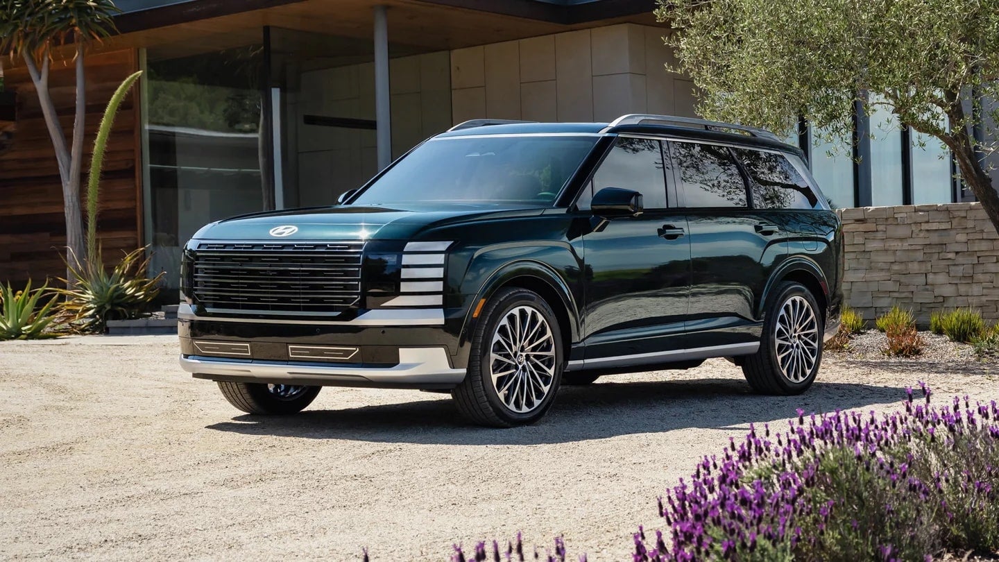 A dark green Hyundai Palisade SUV parked on a street in front of a modern home with lush landscaping.