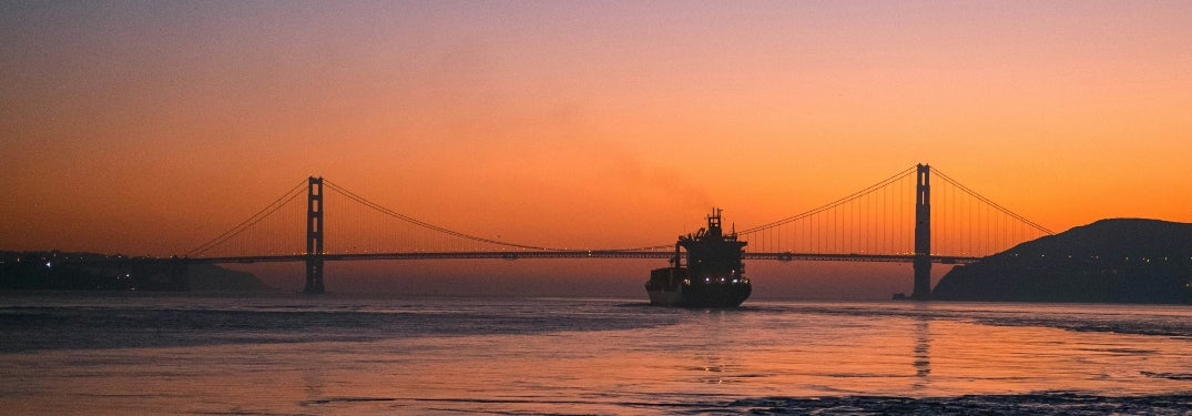 Boat riding by Golden Gate Bridge in sunset