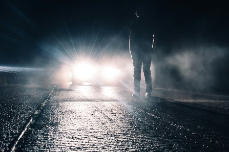 Man standing in front of car with headlights on in the dark