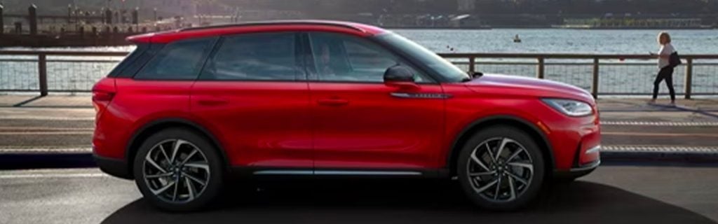 Red Lincoln Corsair SUV driving along a waterfront road, showcasing its sleek profile and modern design.