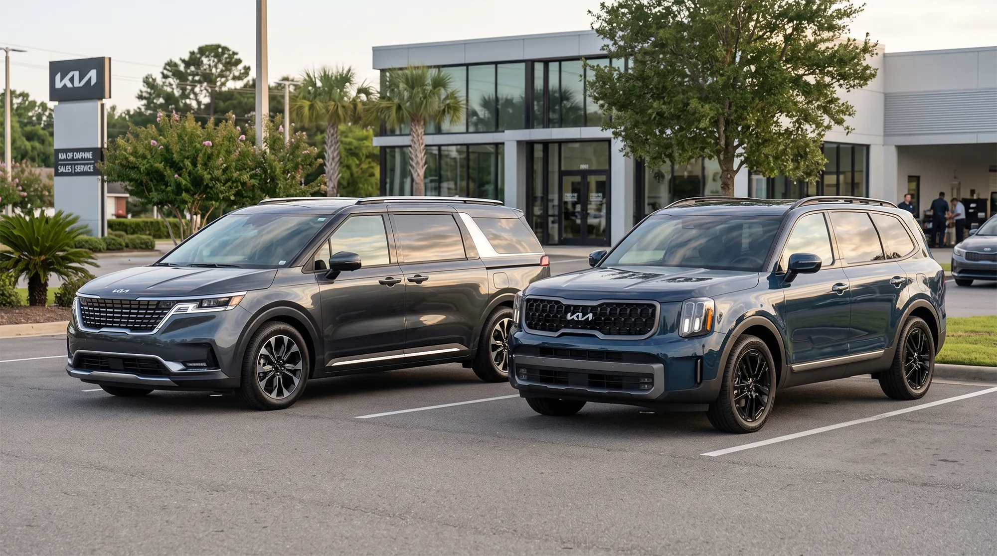 2026 Kia Carnival and 2025 Kia Telluride parked side by side outside Kia of Daphne dealership.