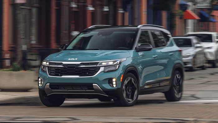 Green Kia Seltos compact SUV driving through a city street