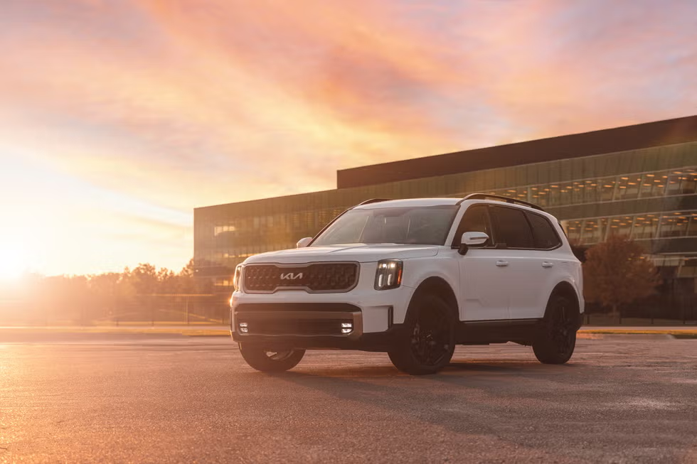 White Kia Telluride SUV parked in front of a modern building at sunset