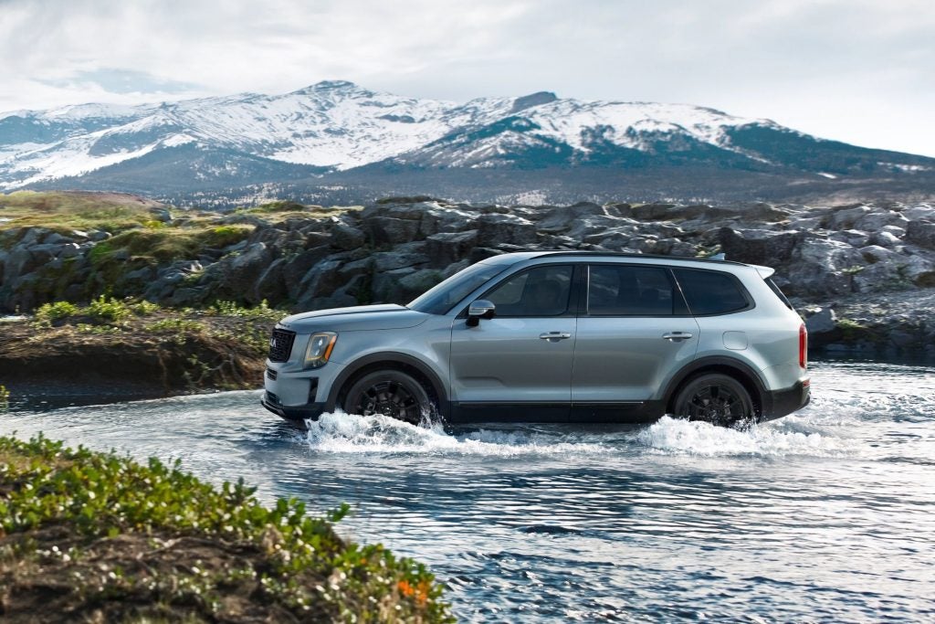 Kia Telluride SUV driving through shallow water with mountains in the background, showcasing rugged capability, all-terrain performance, and advanced safety features.