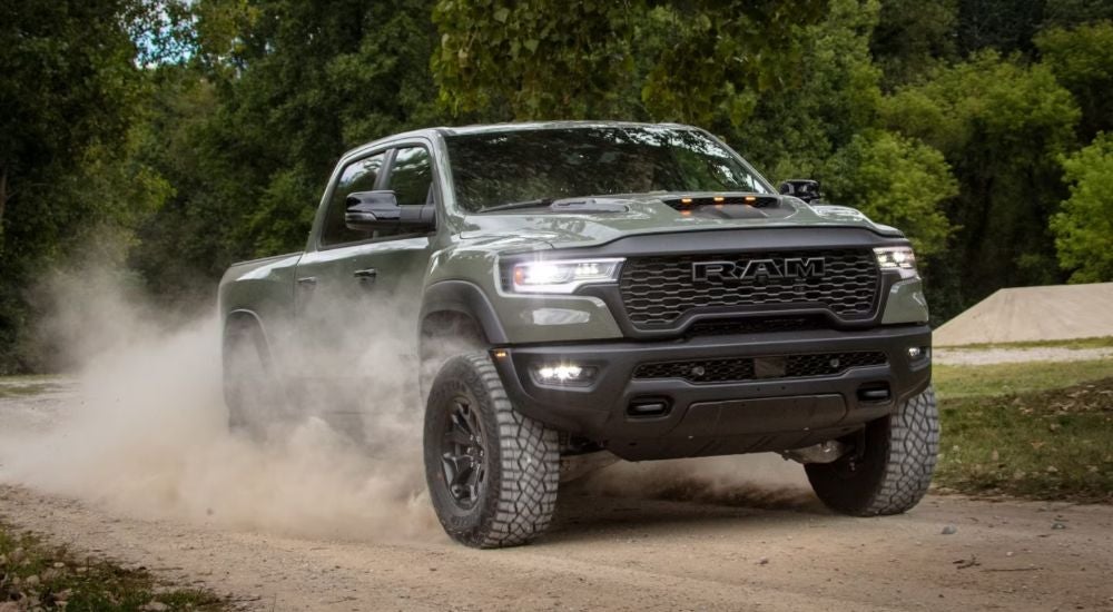 A green 2026 Ram 1500 RHO 4x4 Crew Cab driving a dirt road and kicking up dust.