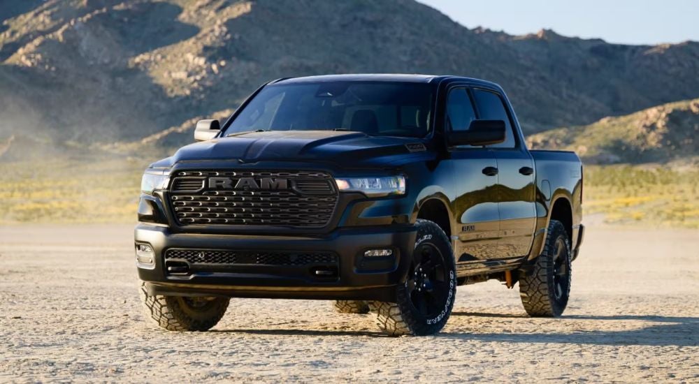 A black 2026 Ram 1500 shown parked on a dirt field by mountains.