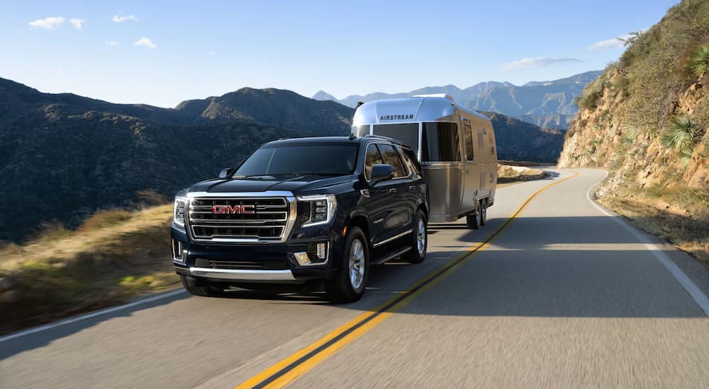 A black 2021 GMC Yukon towing an Airstream down a mountain-lined road.