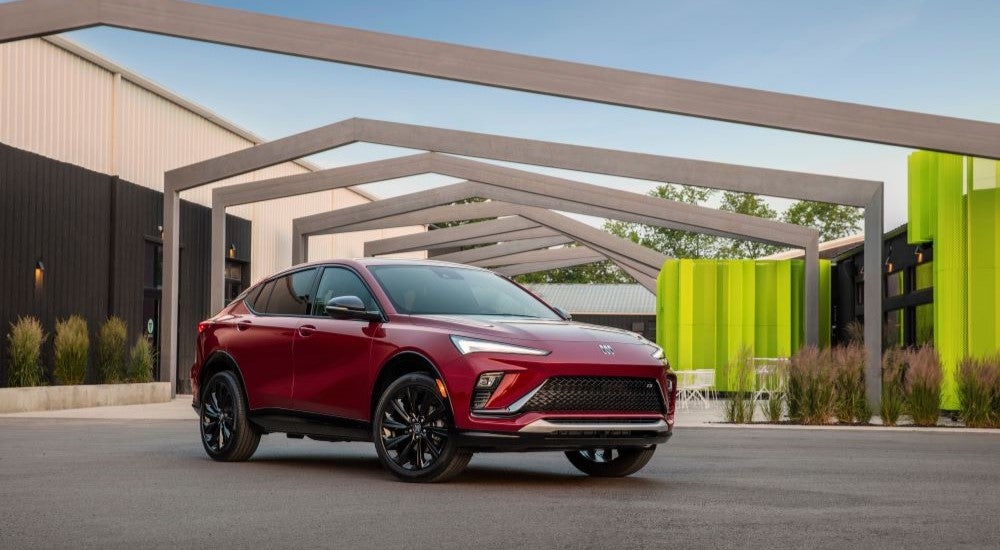 A red 2024 Buick Envista ST is shown in front of a modern building after leaving a Buick dealer near Brighton.
