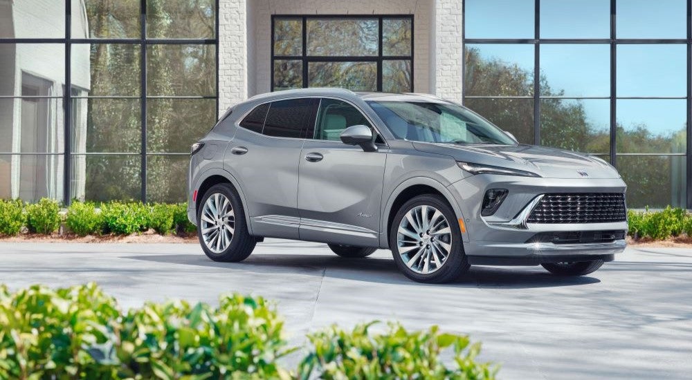 A silver 2024 Buick Envision Avenir parked by a glass building.