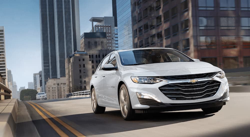 White 2023 Chevy Malibu driving down a city street.