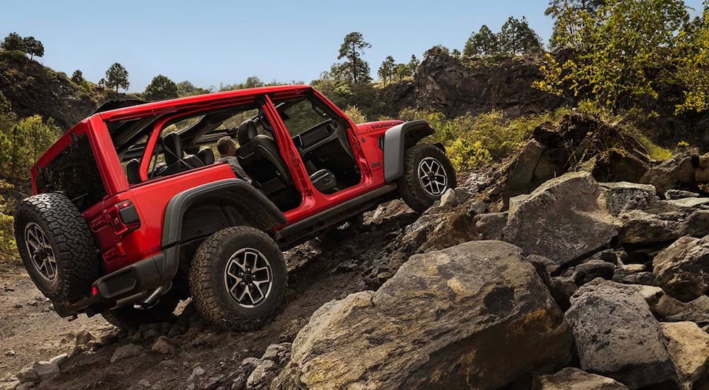 Rear of a red 2026 Jeep Wrangler driving up a hill.