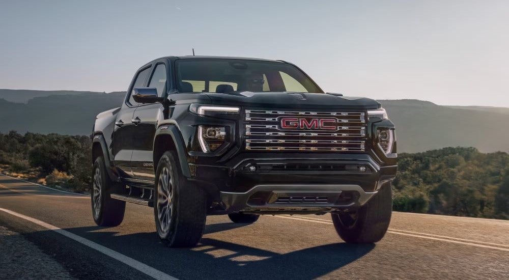 A black 2024 GMC Canyon Denali driving from a GMC dealer near Brighton.