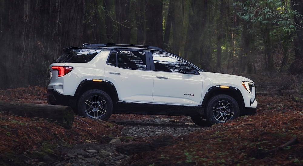 Side of a white 2026 GMC Terrain parked off-road in a forest.