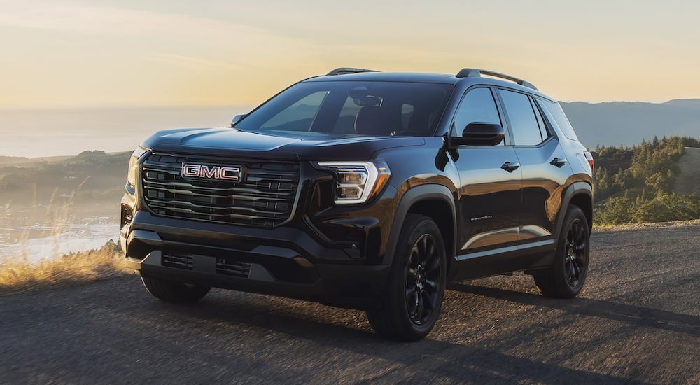 Black 2026 GMC Terrain driving off-road near a lake.