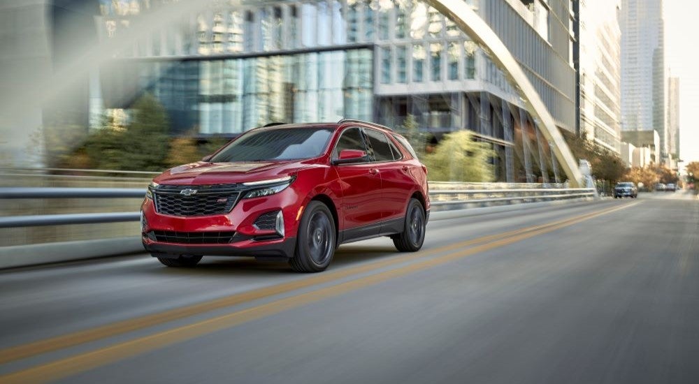A red 2024 Chevy Equinox RS is shown driving over a bridge after leaving a Chevy dealer near Novi.