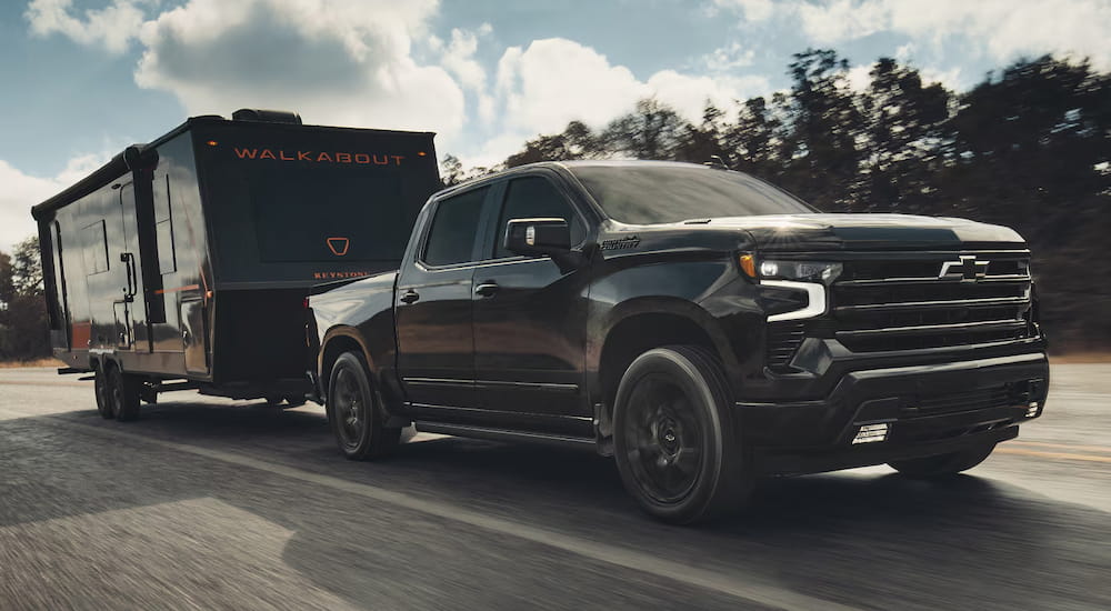 Black 2027 Chevy Silverado 1500 towing a camper down a road.