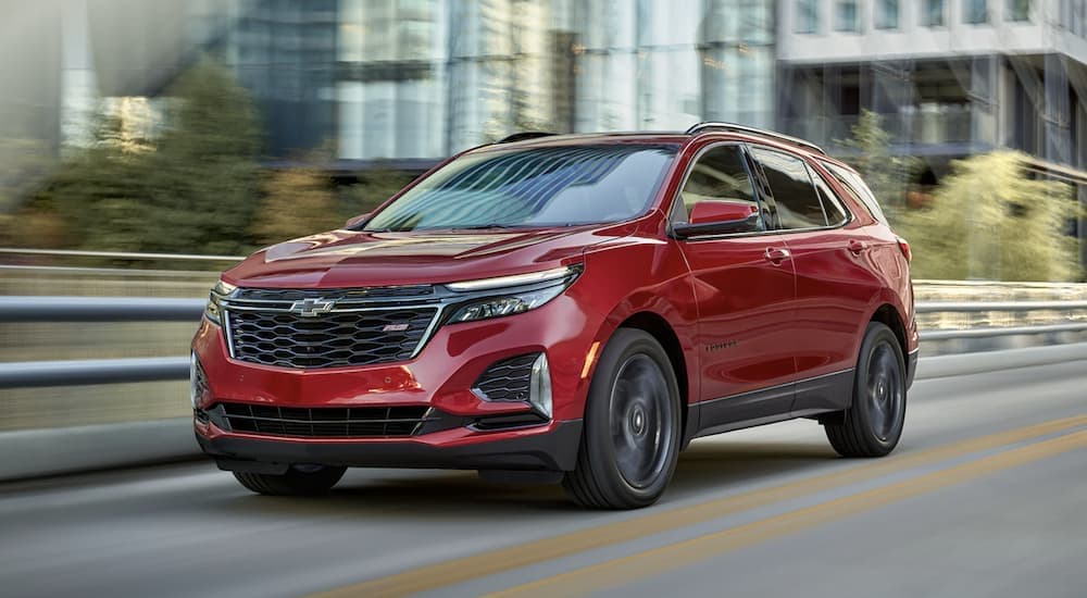 A red 2023 Chevy Equinox RS driving to view a used Chevy for sale.