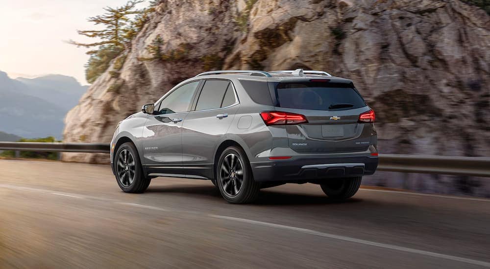 A grey 2024 Chevy Equinox Premier is shown from the rear driving on an open road.