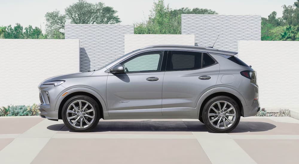Side angle view of a silver 2025 Buick Encore GX parked by a wall.