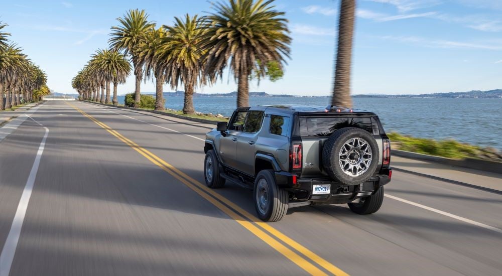 Rear view of a white 2024 GMC Hummer EV driving down a road.