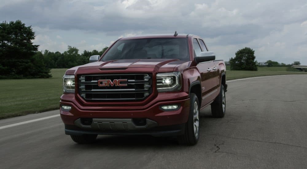 A red 2016 GMC Sierra 1500 driving to a used car dealership.
