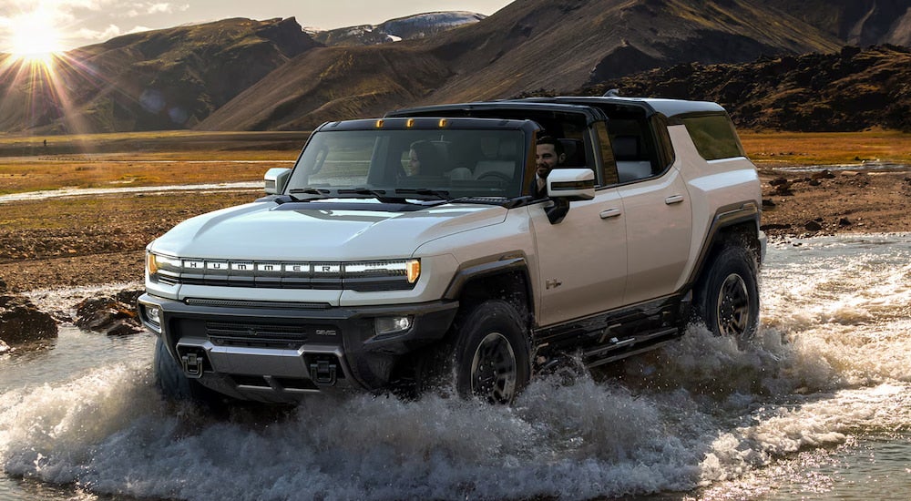 A white 2024 GMC Hummer EV SUV driving through water while off-roading.
